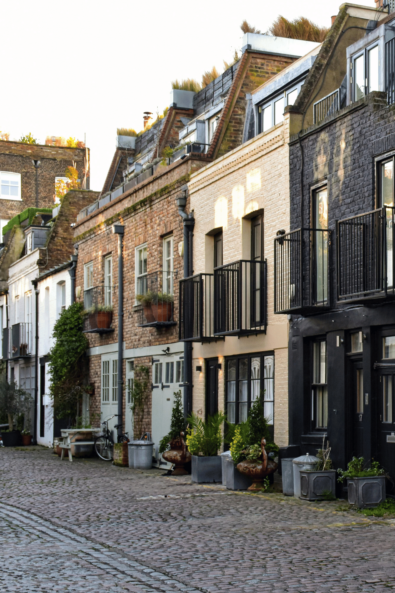 Row of houses with cobbled street, potted plants, and varied brick facades.