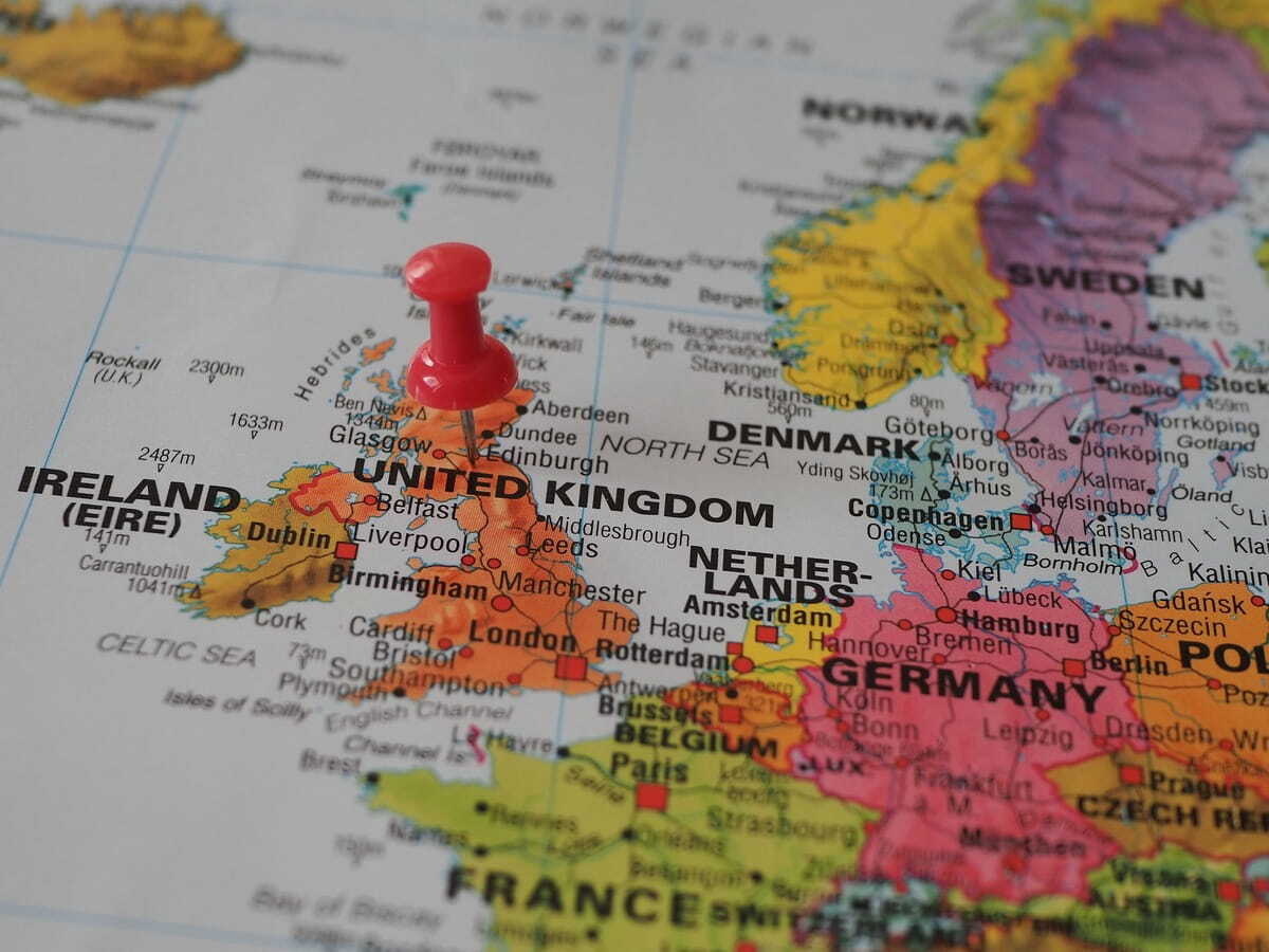 A red push pin stuck into a printed map of Northwestern Europe, pinned near Edinburgh in the United Kingdom.