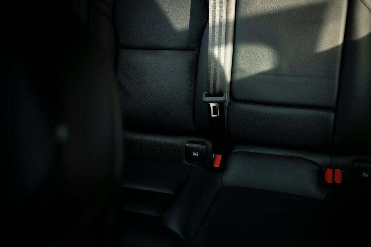 Close-up view of the backseat of a car with black leather upholstery, showing a seatbelt and ISOFIX anchor points for a child seat.