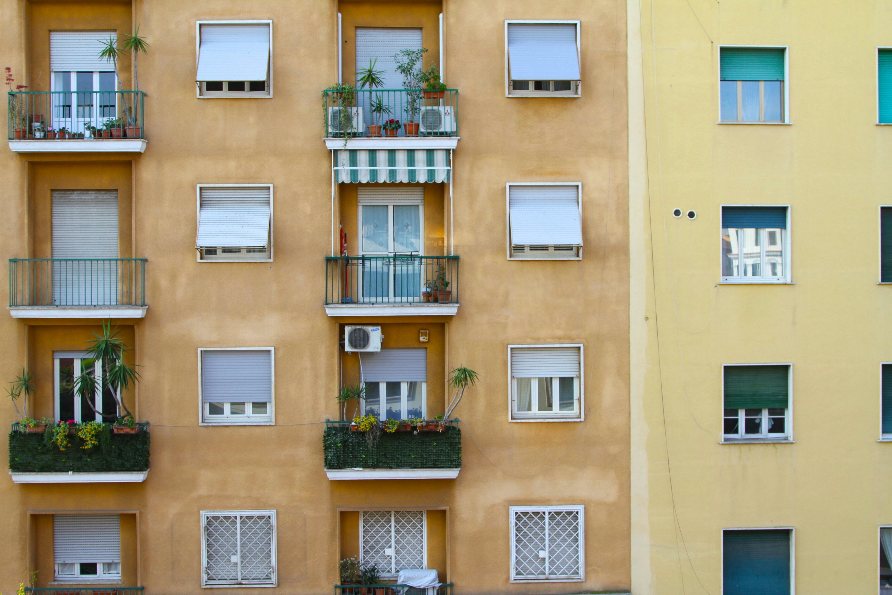 Face-on image of pastel-coloured apartment block with balconies and foliage. 