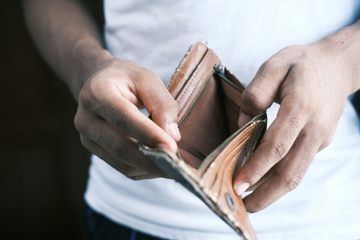 A person holding an empty, worn-out brown wallet with both hands, wearing a white t-shirt, symbolising financial struggle or lack of money.